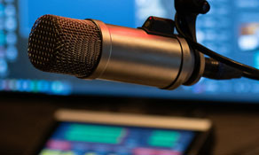 Close up photo of a microphone with broadcasting equipment in the background.